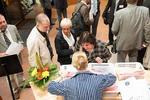 Two people talking to a woman behind a registration desk