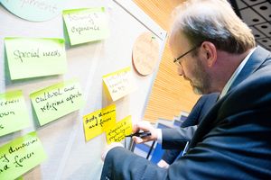 Man putting a hand-written slip of coloured paper on a pinboard